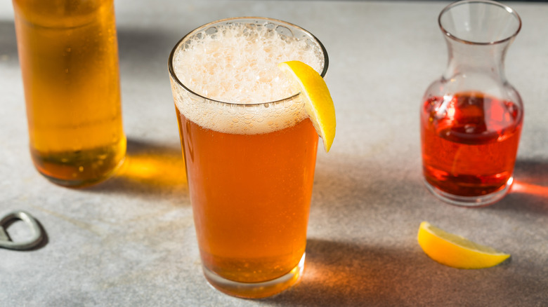 a pint of beer with a lemon slice on the rim and a small decanter of Aperol beside it