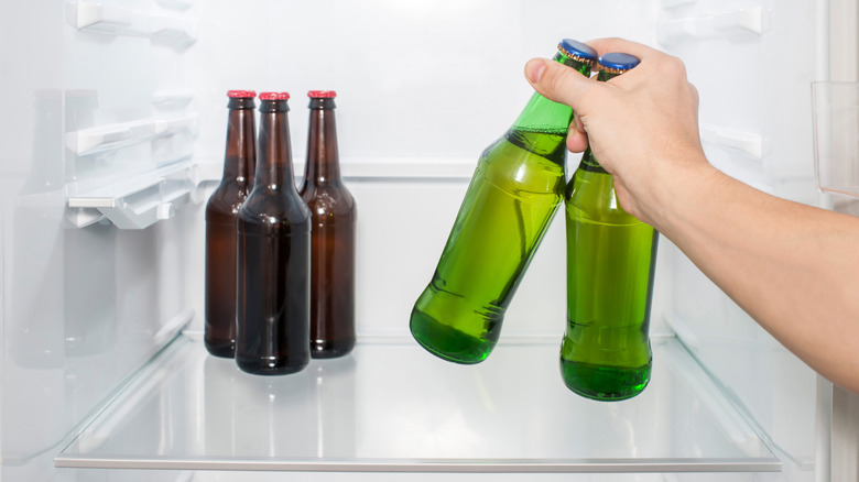 Hand holding two green bottles of beer in the fridge