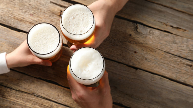 Three hands holding three pint glasses of beer on wooden table