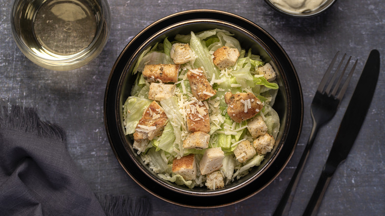 a green salad with croutons and cheese sits in a bowl on a table