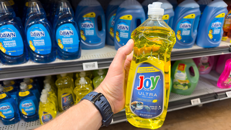 A person holding a bottle of yellow Joy Ultra dishwashing liquid in a store