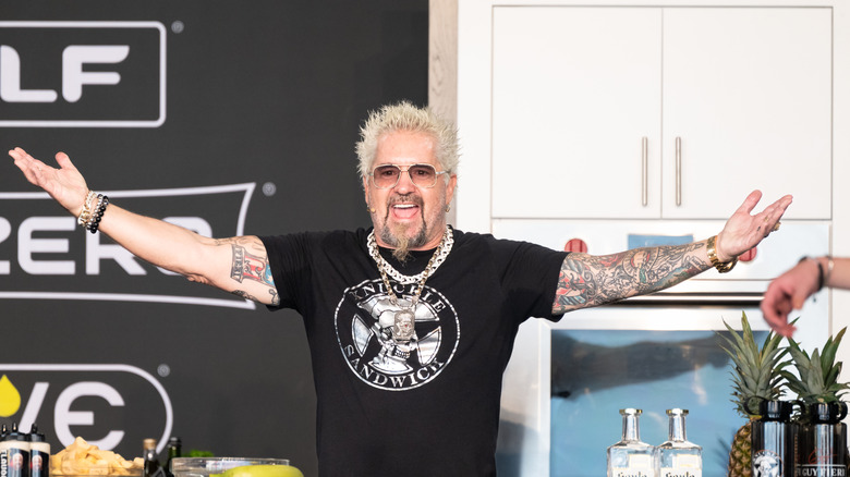 Guy Fieri with his arms extended doing a food demo