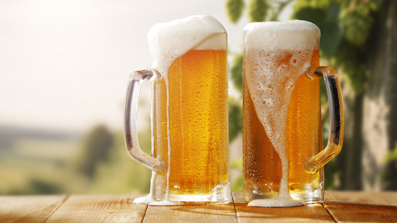 Overflowing mugs of beer on an outdoor wooden table