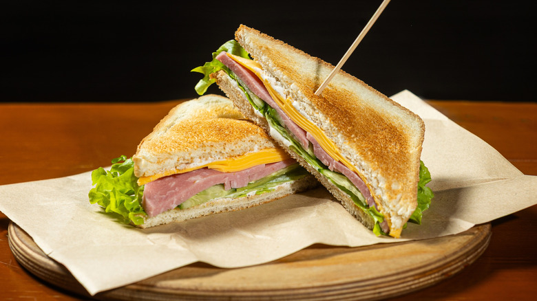 A toasted ham and cheese sandwich with lettuce rests on a white napkin