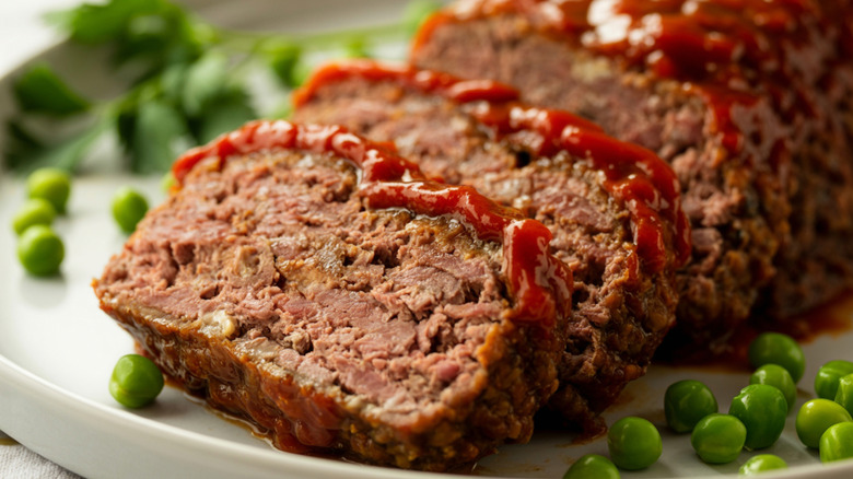 Sliced meatloaf sits on a plate with green peas.