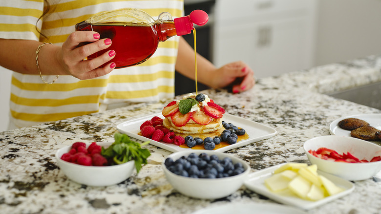pouring syrup over pancakes with fruit and other garnishments