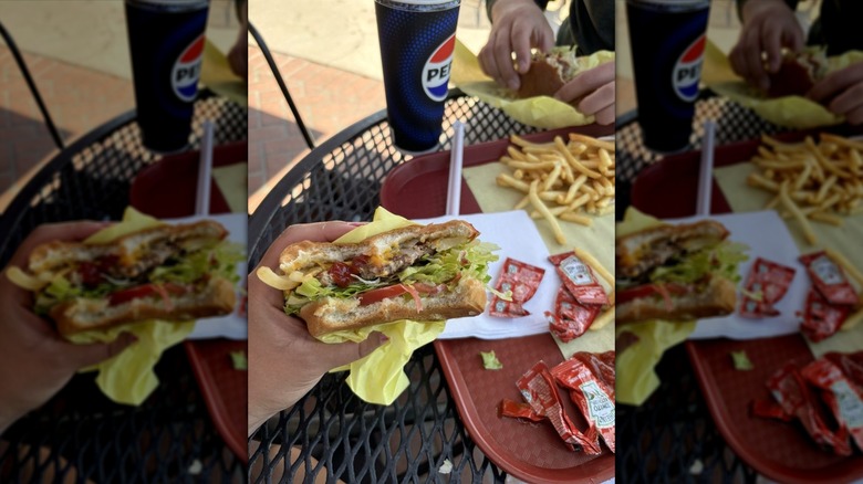 Hand holding a cheeseburger over a tray laden with ketchup packets and fries