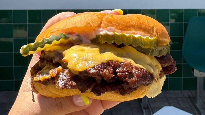 Hand holding a burger loaded with cheese and pickles