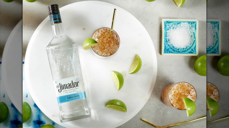 Bottle of El Jimador Silver on a plate with limes and cola cocktails