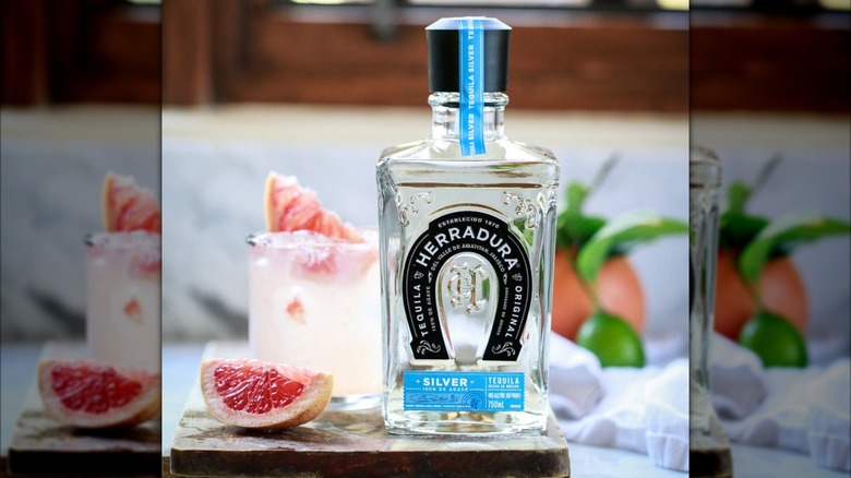 Bottle of Herradura Silver on a board with cocktail and grapefruit slice