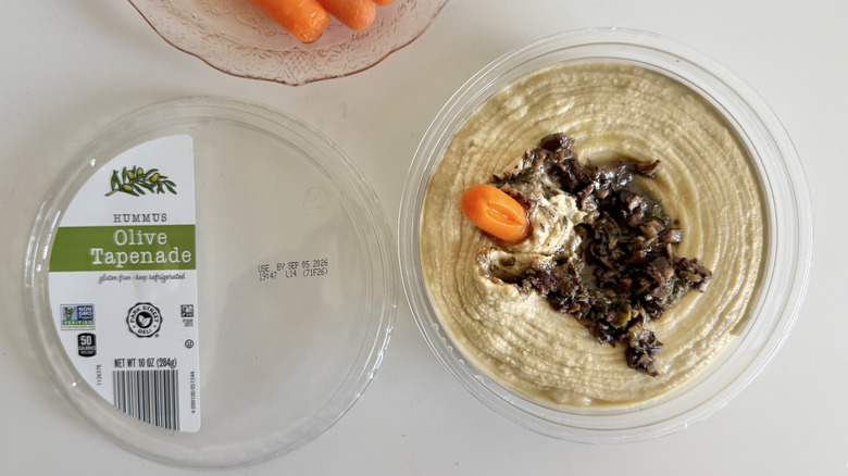 Overhead view of Aldi Olive Tapenade Hummus in a plastic tub served with carrots