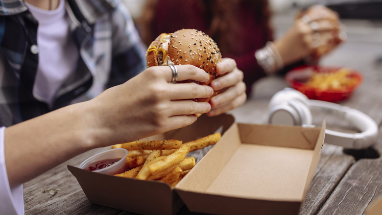A person holding a burger from a fast food box