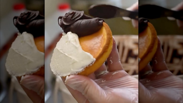 Hand holding a black and white cookie while applying chocolate frosting with a knife