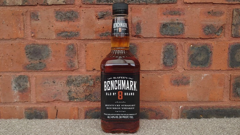 A bottle of Benchmark bourbon next to a filled glass with a red brick background