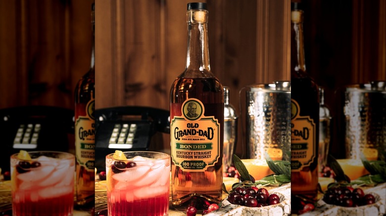 A bottle of Old Grand-Dad Bonded surrounded by fruits and a cocktail, with a wired telephone in the background