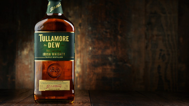 A stylized product shot of a bottle of Tullamore D.E.W. lit up on a wooden surface and background