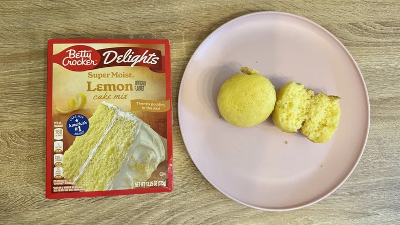 A package of Betty Crocker Delights Lemon Cake Mix next to two cupcakes on a white plate