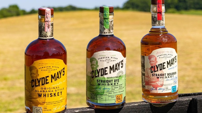 Three bottles of Clyde May's on fence with blurred field background
