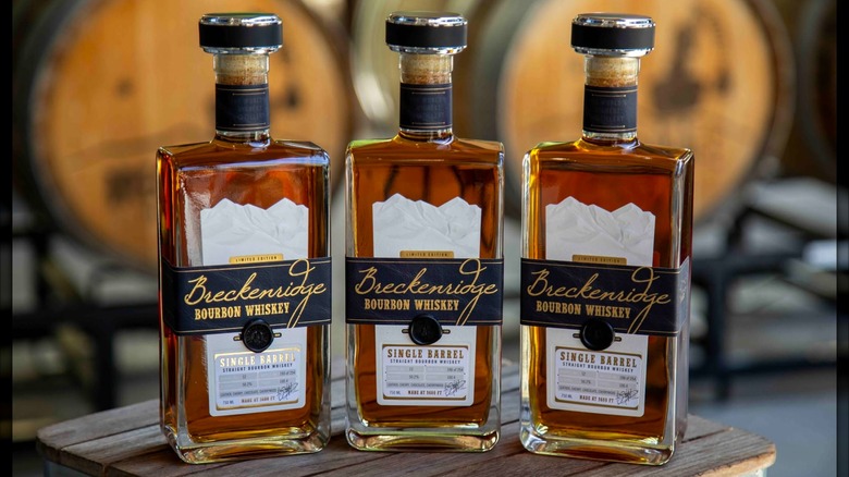 Three bottles of Breckenridge bourbon on wooden tables barrels in background