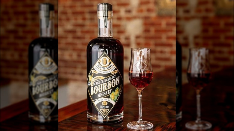 Bottle of Painted Stave bourbon on wooden table with glass