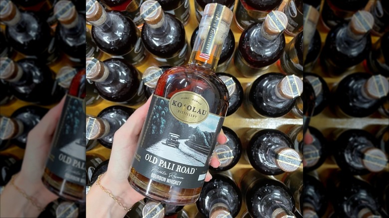 Hand holding Old Pali Road bourbon over other bottles