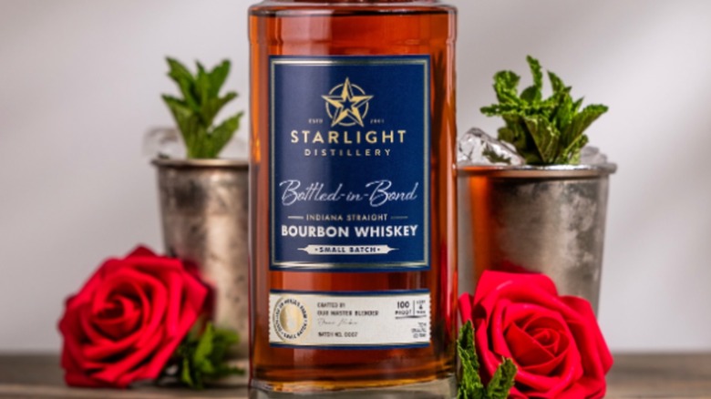 Bottle of Starlight bourbon whiskey with roses and cocktails in background