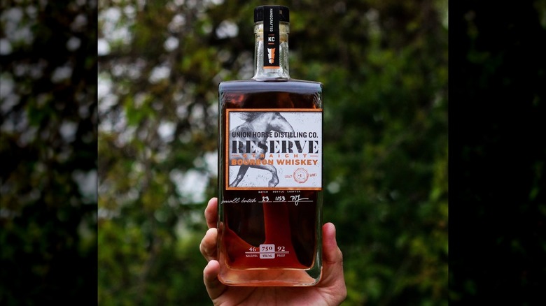 Hand holding bottle of Union Horse whiskey in front of blurred trees
