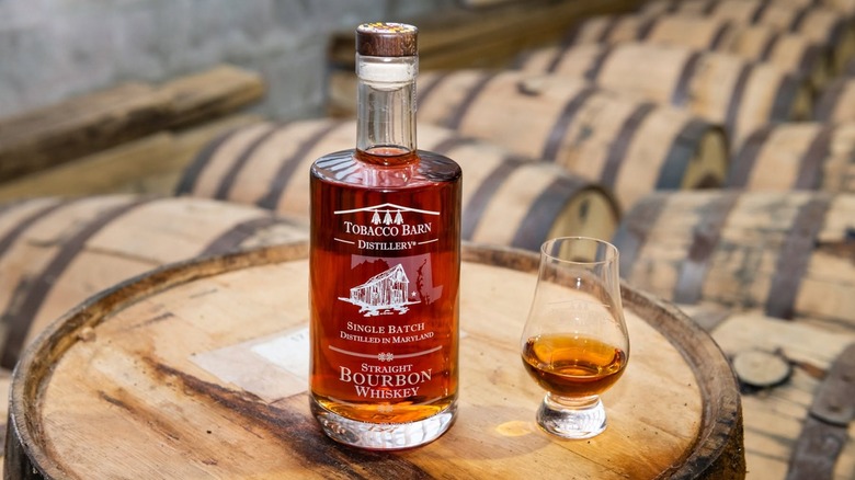 Bottle of Tobacco Barn Distillery bourbon and glass on barrel with more in background