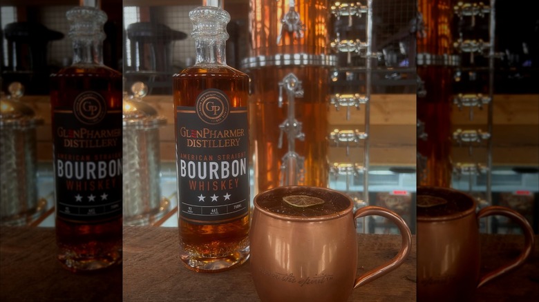Bottle of GlenPharmer bourbon on table with copper mug and still in backgorund