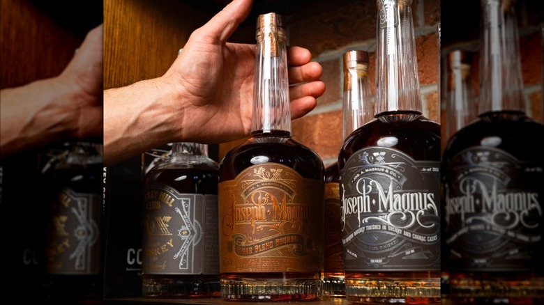 Bottles of bourbon and whiskey from Jos. A Magnus on shelf with hand reaching for one