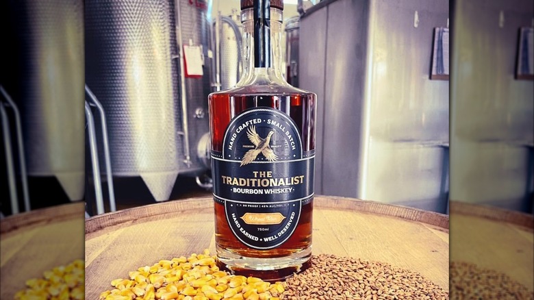 Bottle of The Traditionalist bourbon on barrel with grains