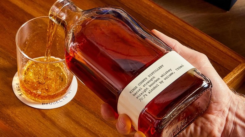 Pouring from a bottle of Kings County bourbon into glass on table
