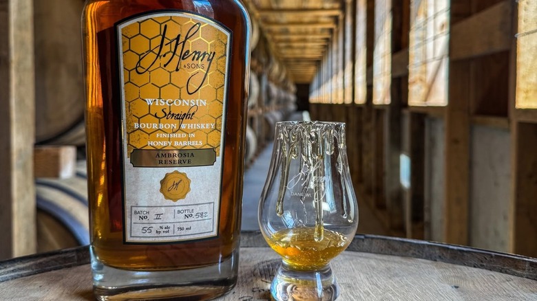 Bottle of honey bourbon with honey in glass on barrel