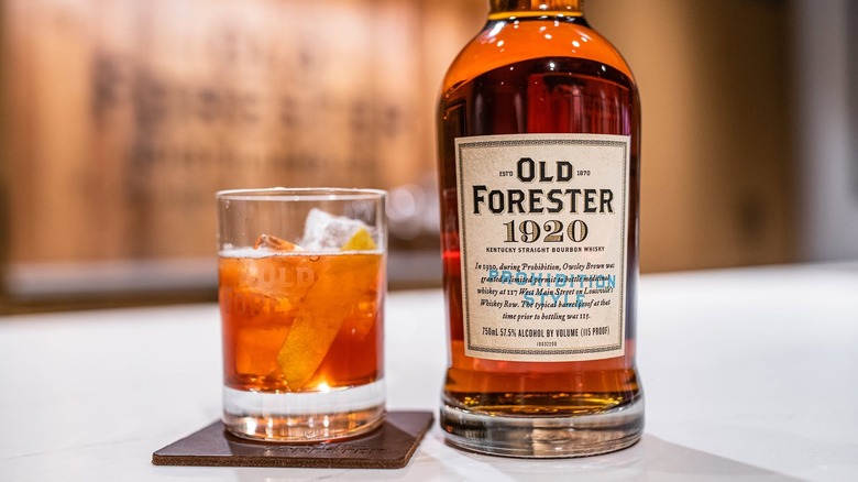 A bottle of Old Forester 1920 placed on a table next to a cocktail