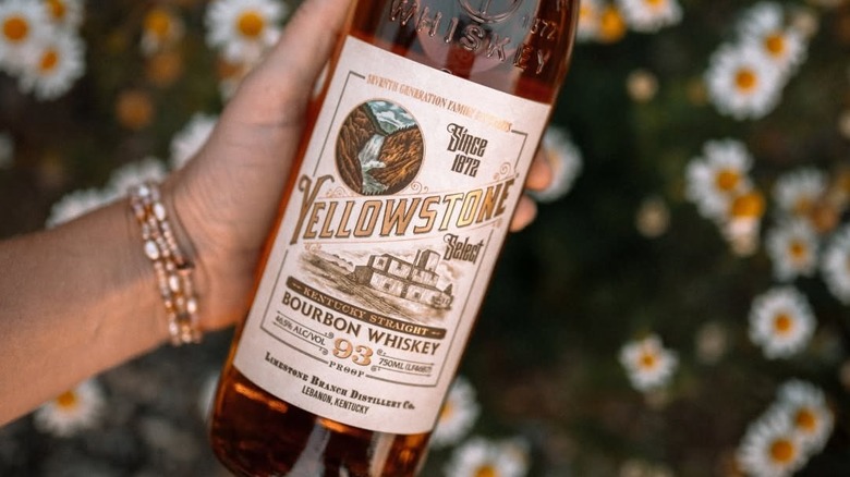 A top-down shot of a bottle of Yellowstone Select Bourbon being shown to camera with flowers in a blurred background