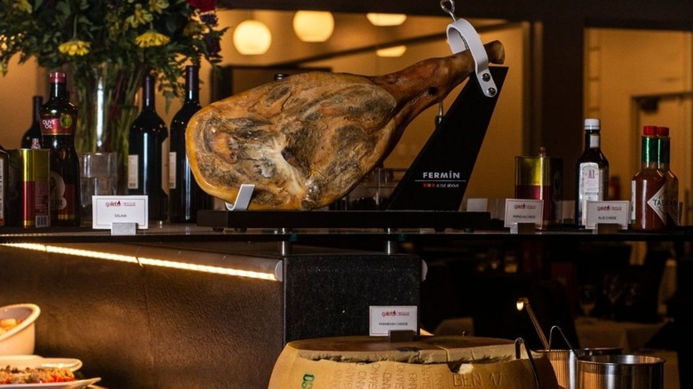 Market table with a jamon leg, cheeses, and bottles of sauces and wines