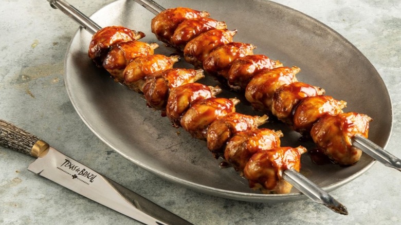 Two chicken skewers on a plate next to a knife