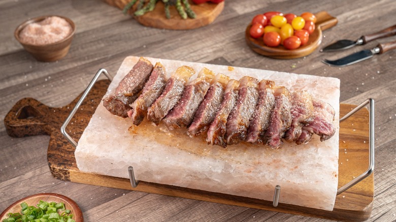 Sliced steak on a wooden board with tomatoes and scallions on the side