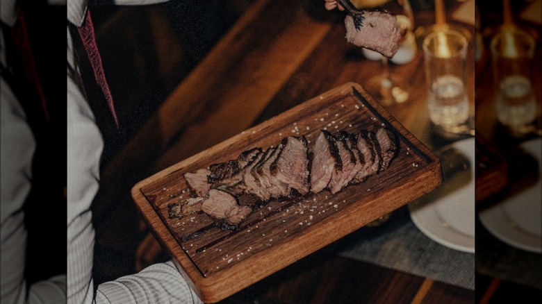 Slices of steak being served off of a wooden platter