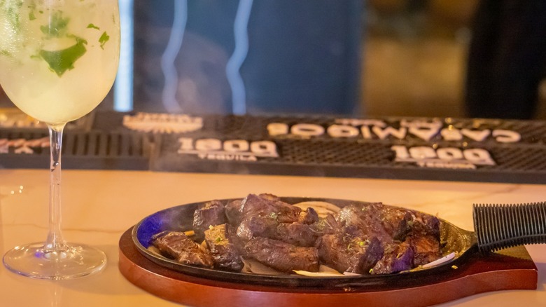 Sizzling steak on a cast-iron pan with a cocktail