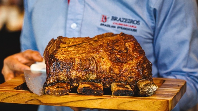 Rack of beef ribs on a wooden tray carried by a server