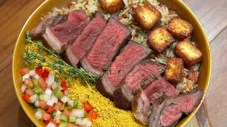 Sliced picanha in a bowl with fried cheese, rice, and diced veg