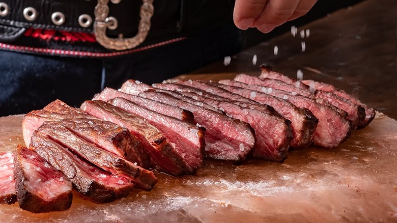 Salt being sprinkled on sliced steak on a salt block