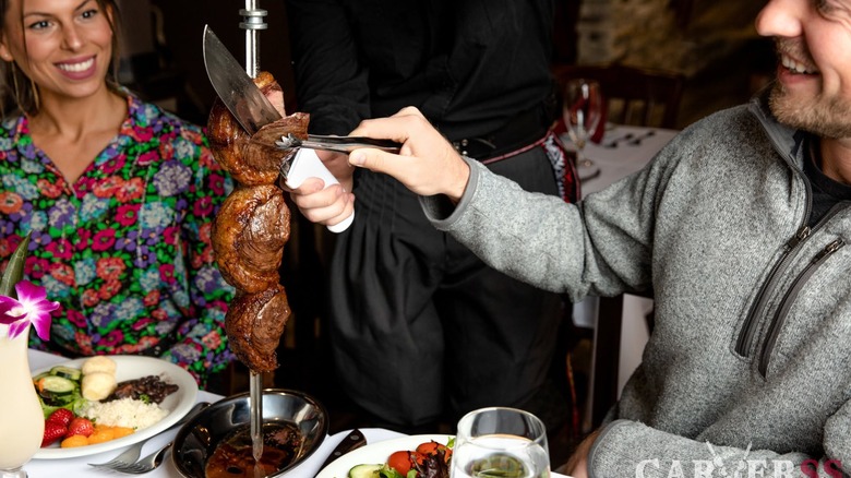 Two happy people carving meat off a skewer