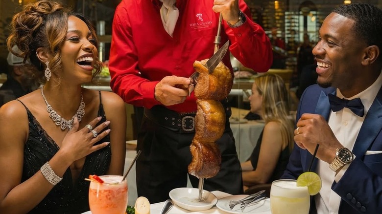 Couple laughing as a server carves meat from a skewer at the table