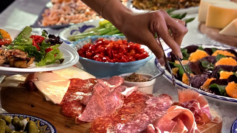 Hand picking up sliced meats from a charcuterie tray on a cold bar