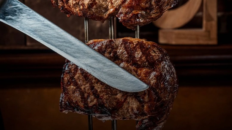 Knife being held in front of steak on skewers