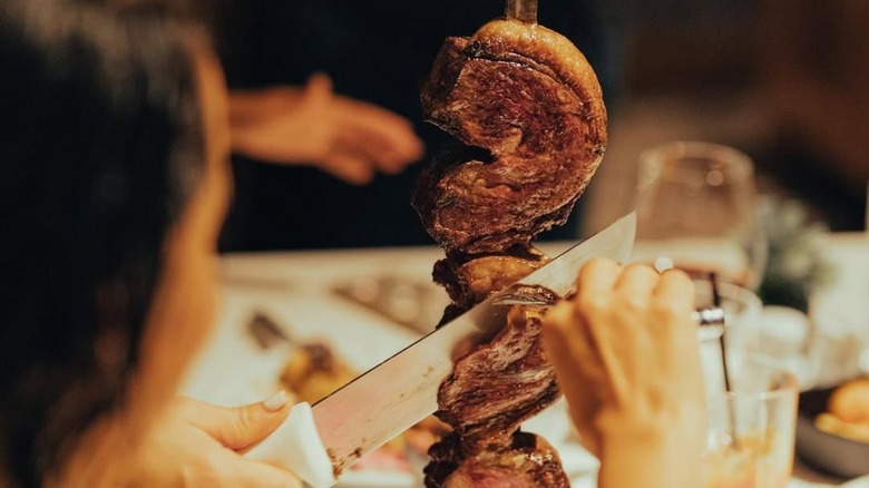 Customer taking a slice of meat from a skewer at a table