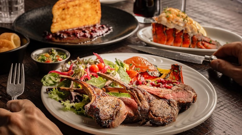 Lamb chops on a plate with salad and lobster in a blurred background