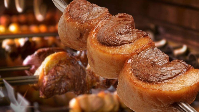 Skewer of steaks in front of a fire and cooking skewers